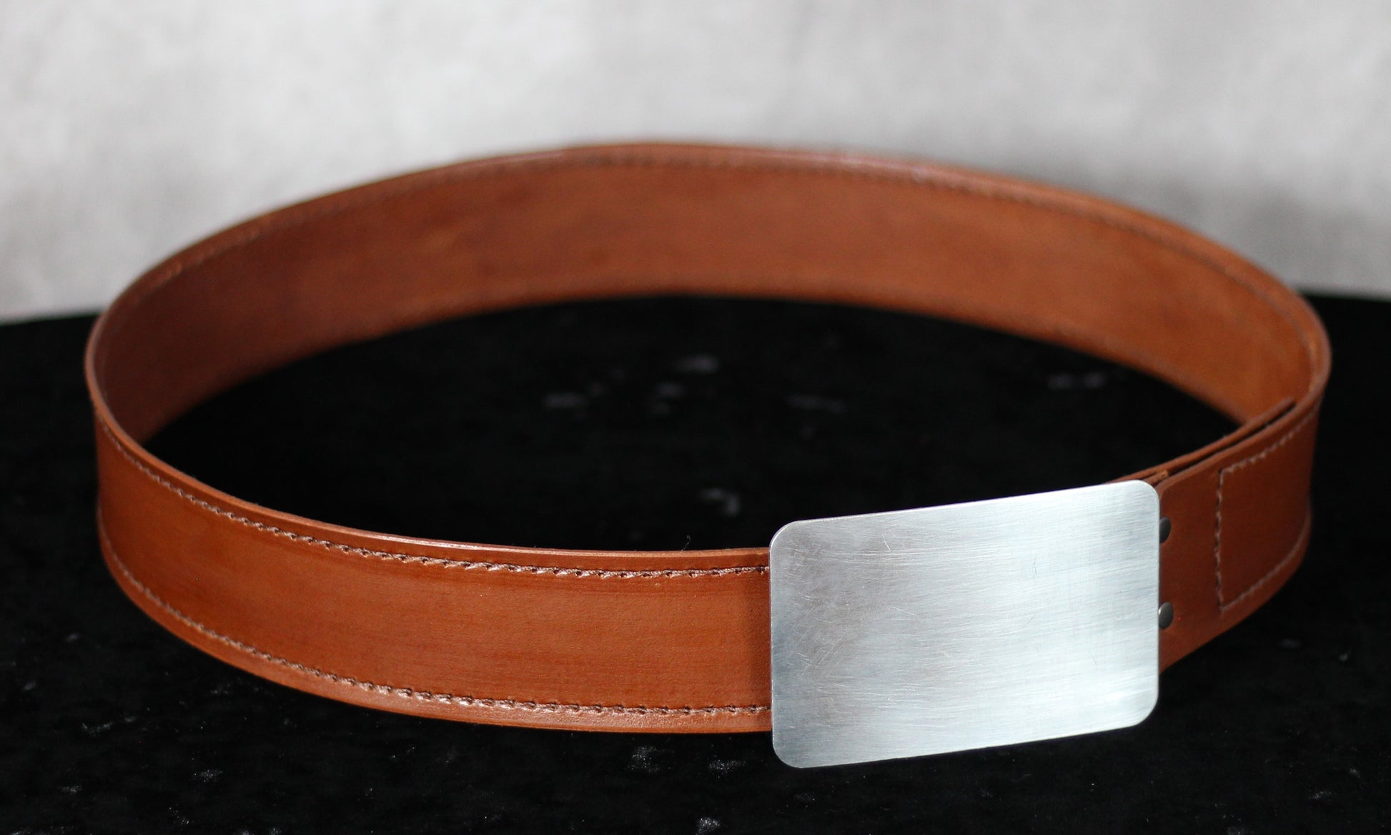 Drifter Series leather belt with machine-stitched detailing and rectangular buckle, approx. 39 inches long, displayed coiled on a grey and black background.